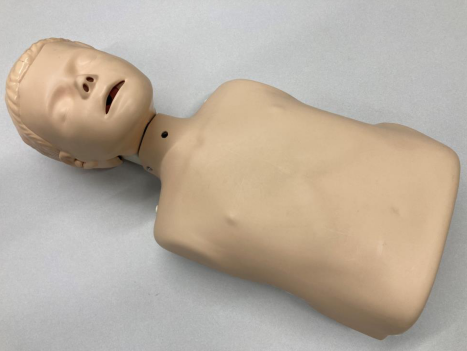 Plastic medical training mannequin showing the upper torso and head used for airway or tracheostomy practice, lying on a flat surface with a smooth, skin‑toned finish and simplified anatomical features.