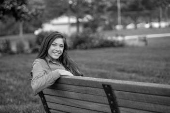 Teenage girl is sitting on a bench outside, smiling
