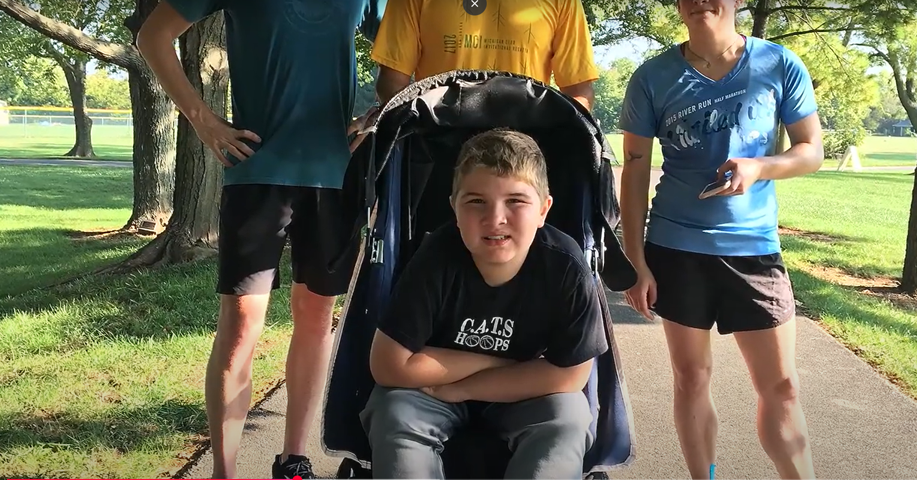 Child sitting in stroller with people standing behind him. 