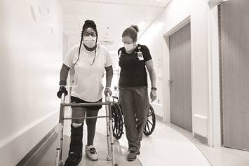 child using a walker, walking down a hallways with a medical professional.