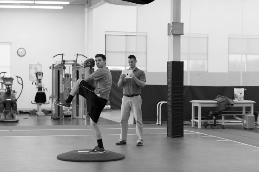 Pitcher practices their throw in a sports medicine facility while an athletic trainer observes.