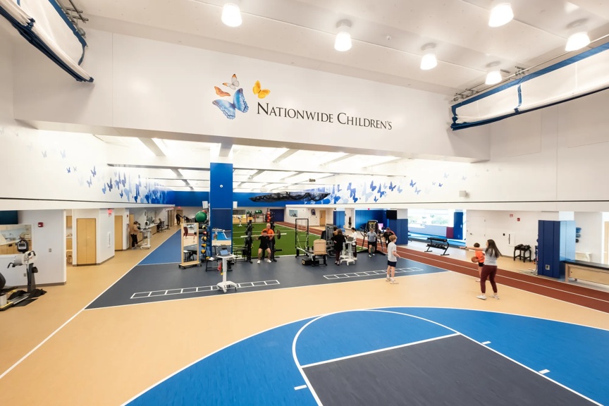 View of a large rehabilitation space in the Livingston Orthopedic and Surgery Center. A basketball court is visible with providers and athletes working together in the background.